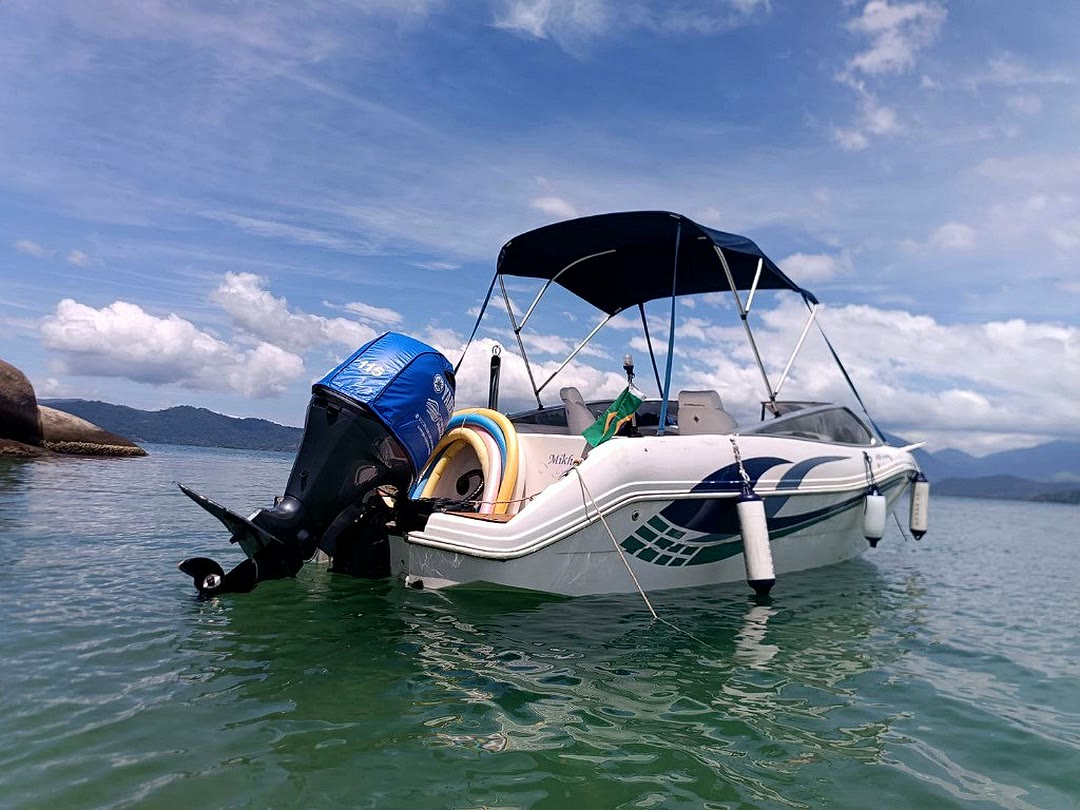 Lancha Mikhael ancorada em água verde em Paraty, com toldo azul e flutuantes coloridos